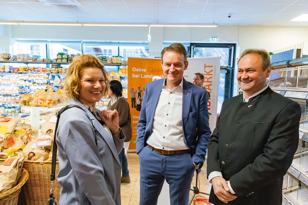Drei Gäste stehen im Verkaufsbereich des SPAR-Marktes Rottenmann und unterhalten sich. Im Hintergrund sind Regale mit Brot und Backwaren sowie Informationsbanner der Landmarkt KG zu sehen. Die Personen lächeln und stehen in entspannter Atmosphäre während der Eröffnungsveranstaltung im Markt.