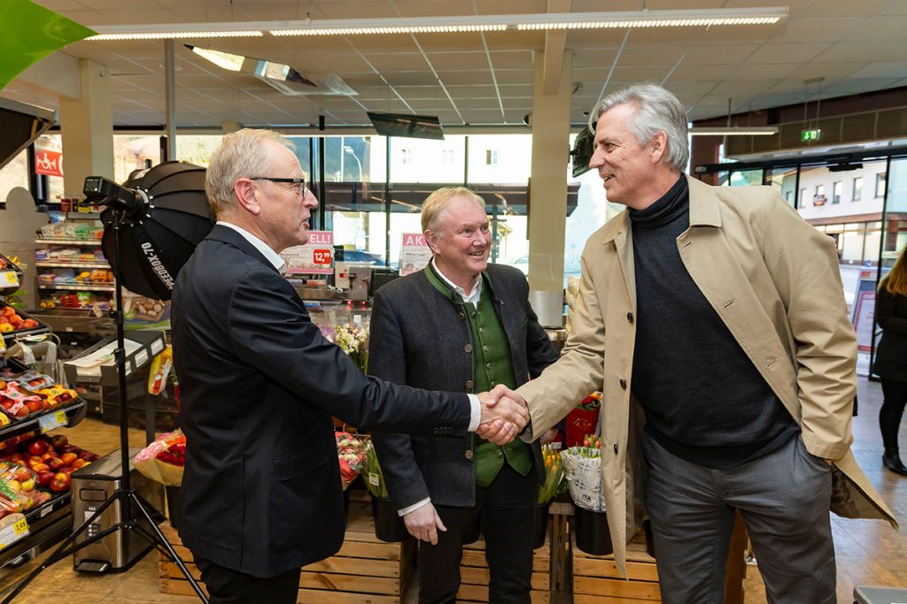 Der Geschäftsführer der Landmarkt KG begrüßt im Verkaufsbereich des SPAR-Marktes Rottenmann den Geschäftsführer der Ennstal Milch mit einem Handschlag. Daneben steht der Vorstandsvorsitzende der Landgenossenschaft Ennstal. Im Hintergrund sind Blumenstände und Verkaufsregale des Marktes zu sehen.