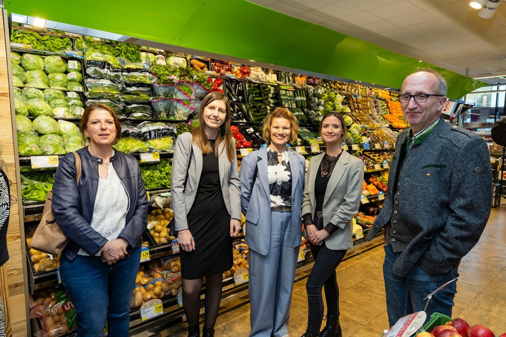 Fünf Gäste der Eröffnungsfeier stehen im Obst- und Gemüsebereich des SPAR-Marktes Rottenmann vor gefüllten Regalen mit frischem Gemüse und Obst und blicken in die Kamera. Die Gruppe steht zwischen den Verkaufsregalen im Markt und unterhält sich in entspannter Atmosphäre.