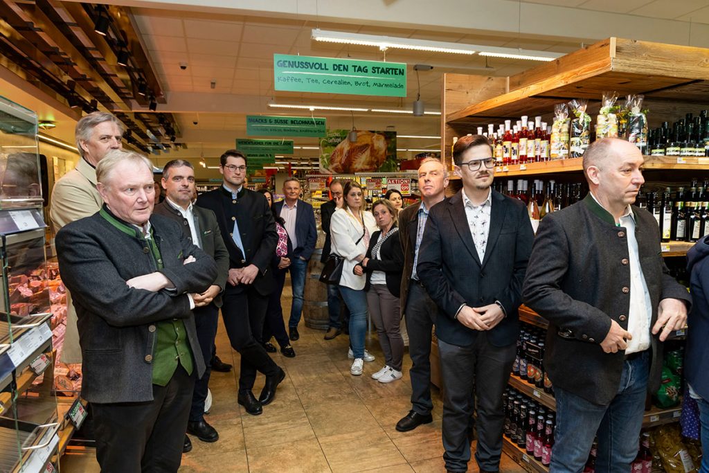 Mehrere Gäste der Eröffnungsfeier stehen im Verkaufsbereich des SPAR-Marktes Rottenmann zwischen den Regalen und hören aufmerksam zu. Im Hintergrund sind Verkaufsregale mit Lebensmitteln sowie Beschilderungen zu verschiedenen Warengruppen zu sehen.
