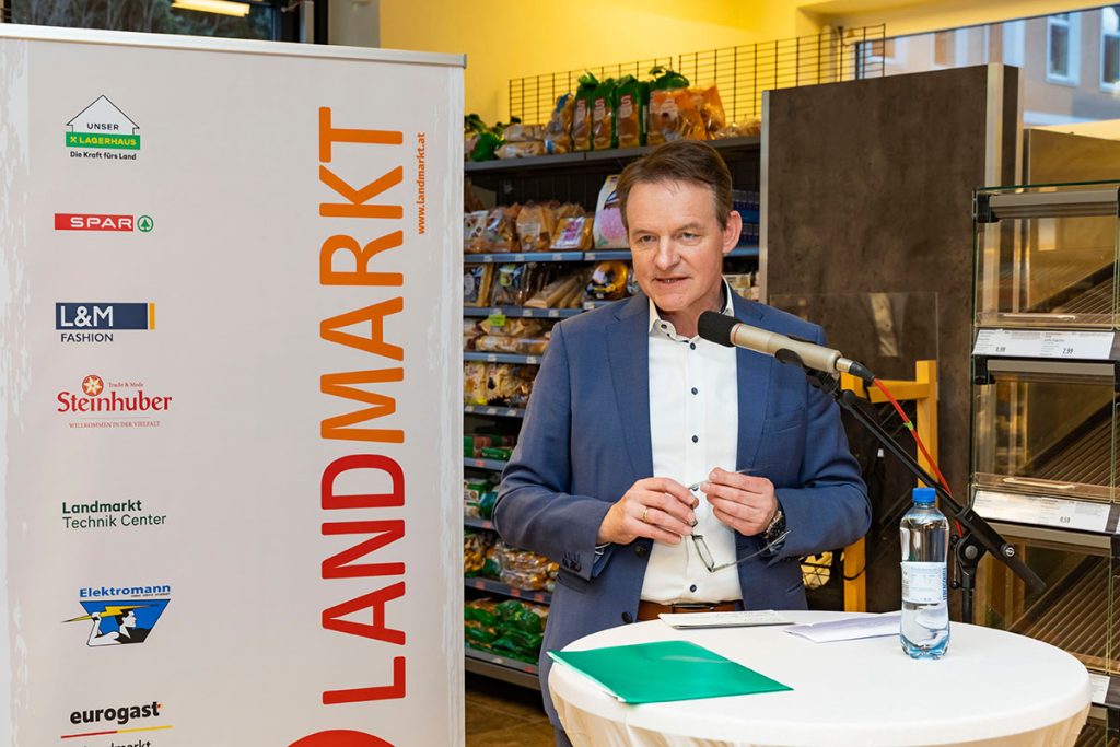 Der Bereichsleiter Landmarkt SPAR hält während der Eröffnungsfeier eine Ansprache im SPAR-Markt Rottenmann. Er steht an einem Stehtisch mit Mikrofon, daneben ein Banner der Landmarkt KG. Im Hintergrund sind Verkaufsregale mit Lebensmitteln zu sehen.