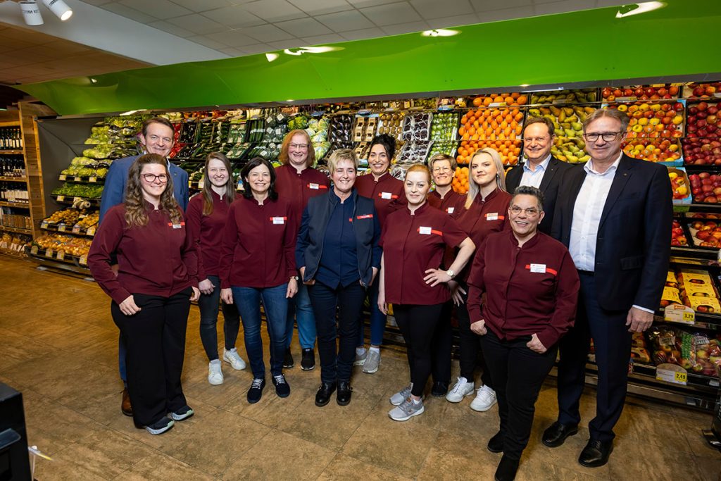 Gruppenfoto des Teams des SPAR-Marktes Rottenmann gemeinsam mit Vertretern der Landmarkt KG und SPAR. Die Mitarbeiterinnen und Mitarbeiter stehen im Obst- und Gemüsebereich vor gefüllten Regalen mit frischem Obst und Gemüse. In der Mitte steht die Marktleiterin, umgeben vom Team in roten SPAR-Uniformen sowie zwei Herren aus der Geschäftsführung.