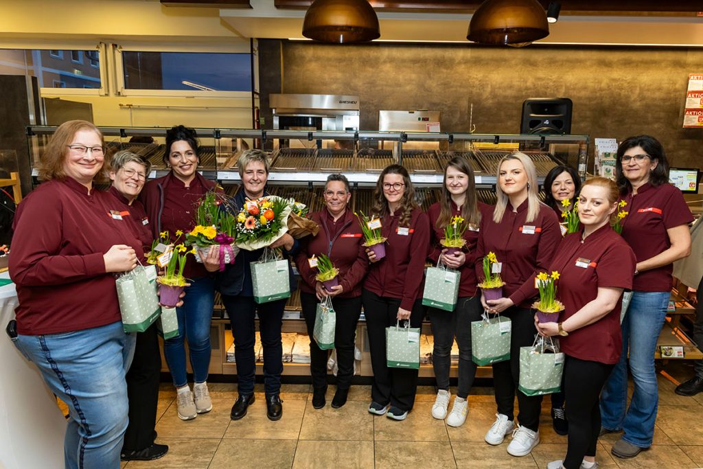 Das Team des SPAR-Marktes Rottenmann steht gemeinsam vor der Backwarenabteilung für ein Gruppenfoto. Die Mitarbeiterinnen tragen SPAR-Arbeitskleidung und halten Blumen sowie kleine Geschenktaschen in den Händen, die ihnen im Rahmen der Feier überreicht wurden.