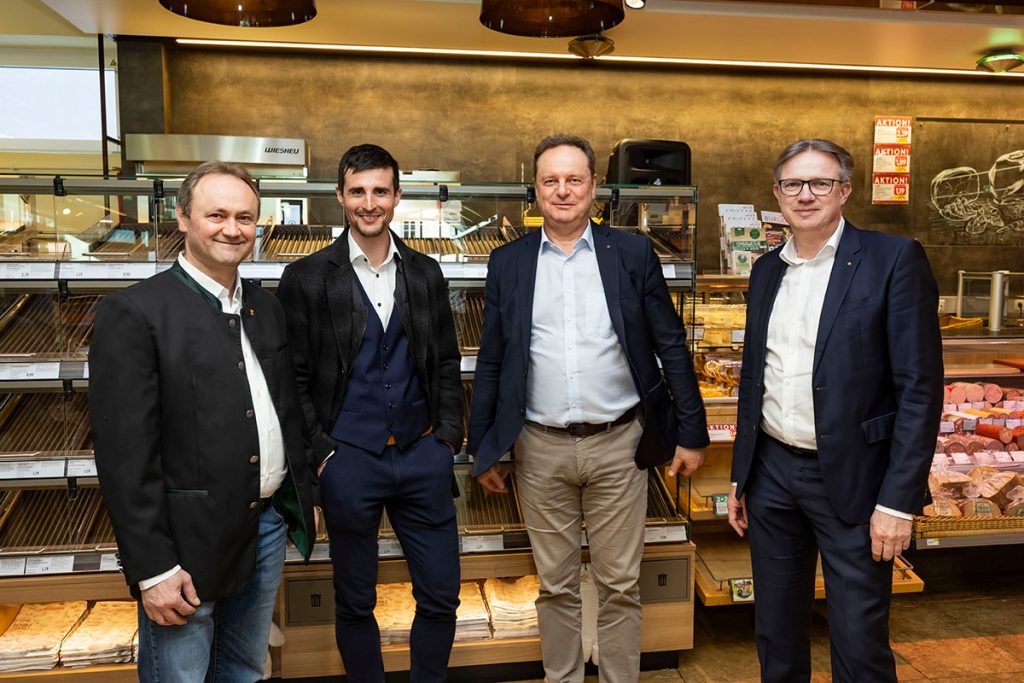 Das Team des SPAR-Marktes Rottenmann steht gemeinsam im Obst- und Gemüsebereich vor gefüllten Regalen mit frischem Obst und Gemüse. In der Mitte halten zwei Personen eine große Eröffnungstorte mit SPAR-Logo und der Aufschrift „SPAR Rottenmann“. Um sie herum stehen Mitarbeiterinnen und Mitarbeiter des Marktes in roten SPAR-Uniformen sowie Vertreterinnen und Vertreter des Unternehmens.