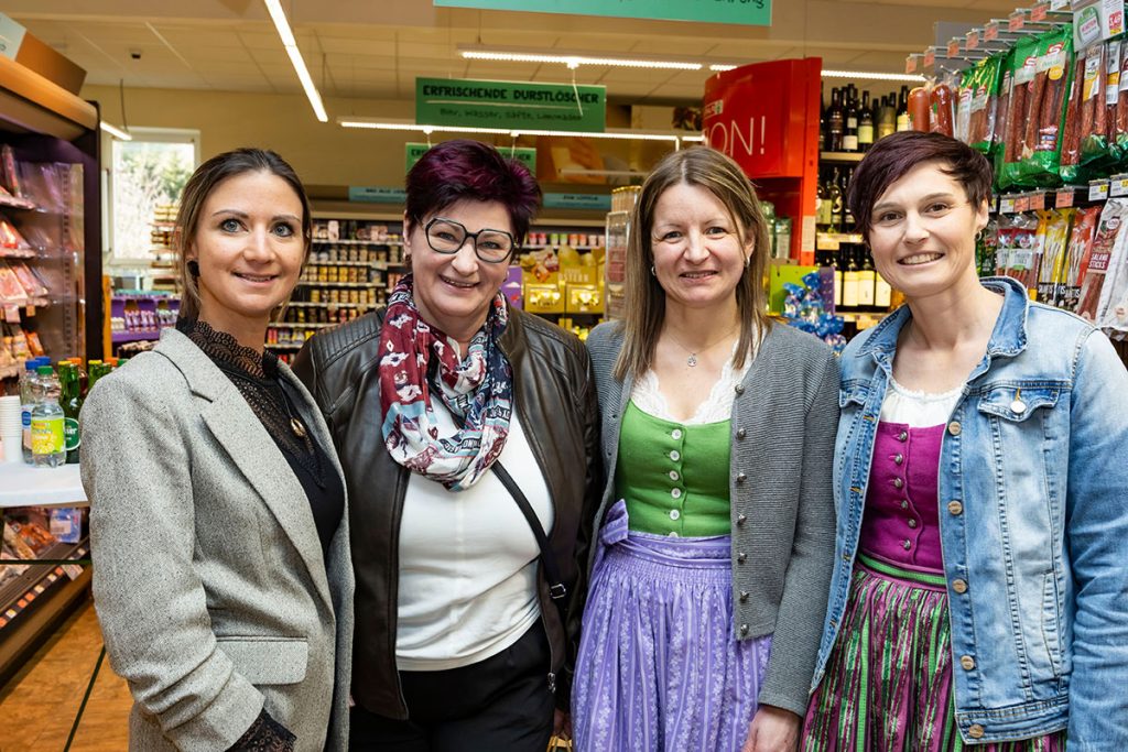 Vier Frauen stehen in einem SPAR-Supermarkt zwischen den Regalen und lächeln in die Kamera. Zwei der Frauen tragen traditionelle Dirndl, während die anderen moderne Kleidung tragen. Im Hintergrund sind Verkaufsregale mit Getränken, Lebensmitteln und regionalen Produkten zu sehen.