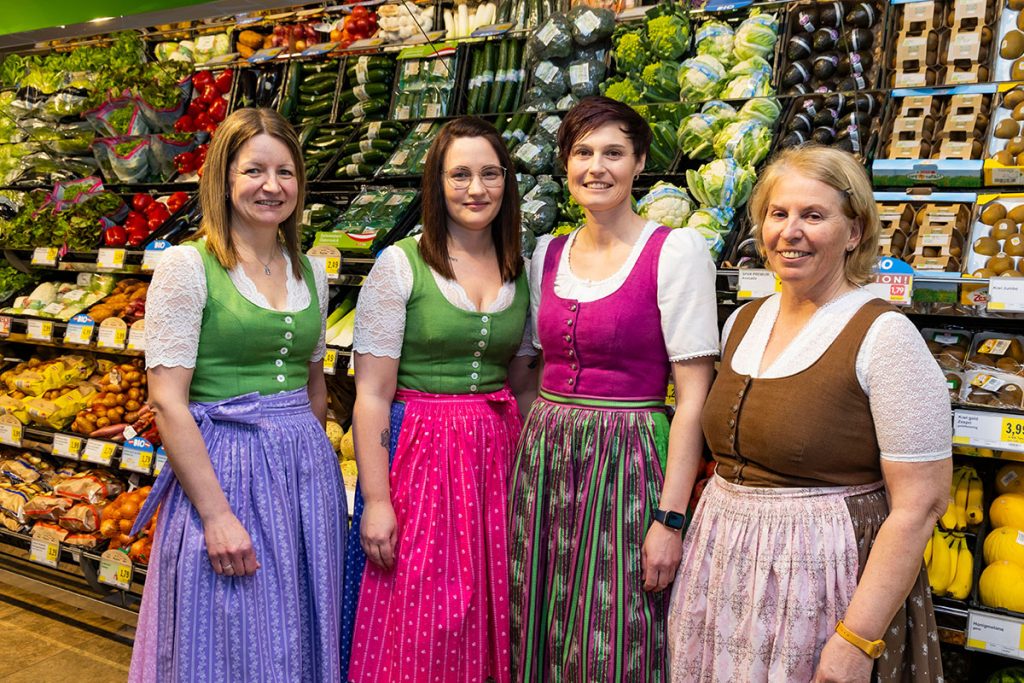 Vier Mitarbeiterinnen stehen im Obst- und Gemüsebereich des SPAR-Marktes Rottenmann vor gefüllten Regalen mit frischem Gemüse und Obst. Sie tragen traditionelle Dirndl in verschiedenen Farben und lächeln in die Kamera.