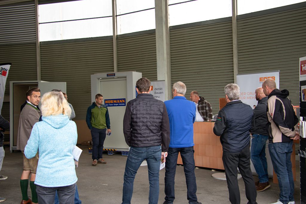 Mehrere Besucher verfolgen beim Kompetenztag in Aigen eine Präsentation am Eder-Stand. Im Hintergrund sind außerdem Ausstellungsbereiche von Hörmann und weiteren Partnern zu sehen.