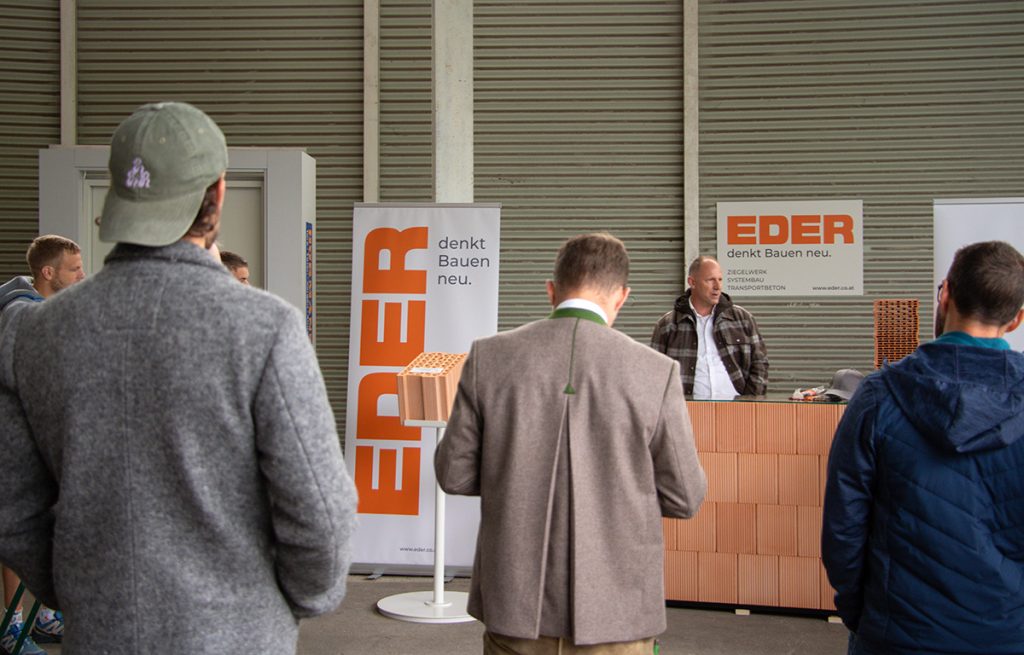 Mehrere Besucher verfolgen beim Kompetenztag in Aigen eine Präsentation am Eder-Stand mit verschiedenen Ziegeln und Baustoffmustern.