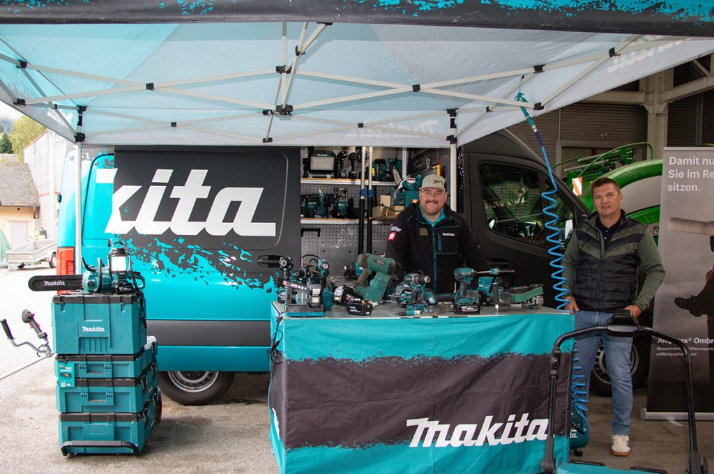 Zwei Fachberater stehen beim Kompetenztag in Aigen am Makita-Stand vor einem Präsentationstisch mit verschiedenen Akkuwerkzeugen und Maschinen.