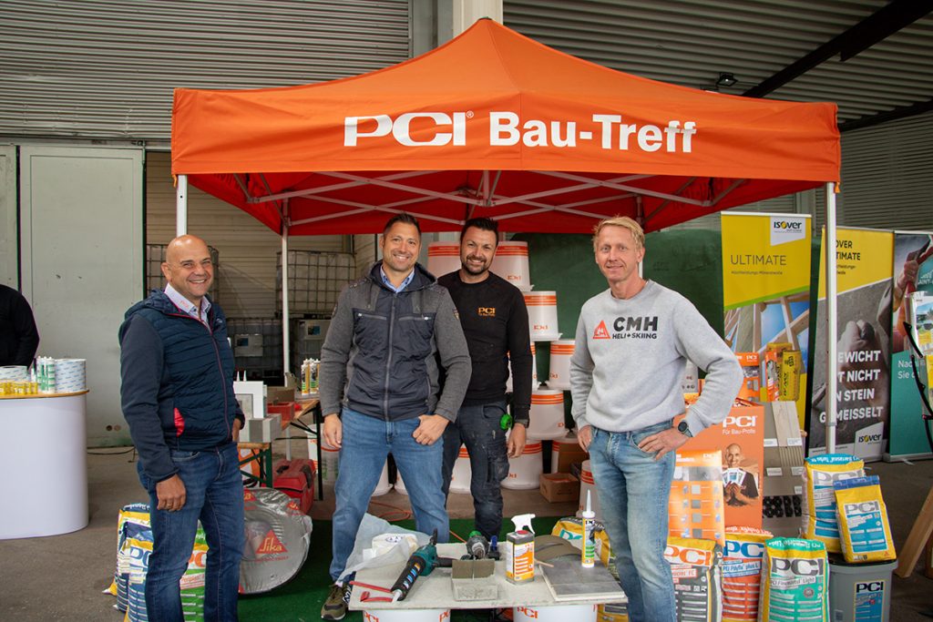 Vier Teilnehmer stehen beim Kompetenztag in Aigen gemeinsam am PCI Bau-Treff. Rund um den Stand sind verschiedene Baustoffprodukte und Informationsmaterialien ausgestellt.