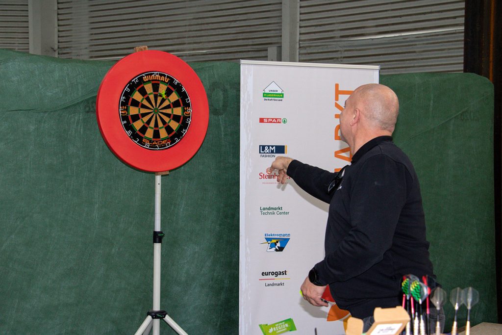 Ein Besucher wirft beim Kompetenztag in Aigen einen Dartpfeil auf die Dartscheibe und nimmt an einer der Challenges des Tages teil.