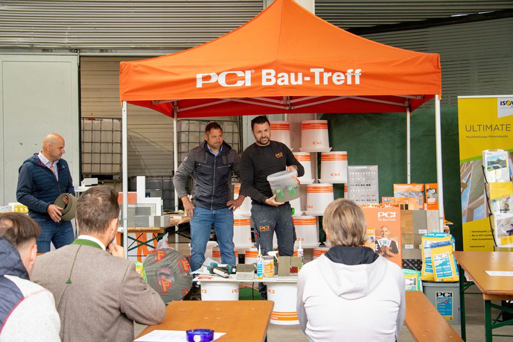 Ein PCI-Fachberater präsentiert beim Kompetenztag in Aigen verschiedene Baustoffprodukte und Anwendungslösungen vor mehreren Besucherinnen und Besuchern.