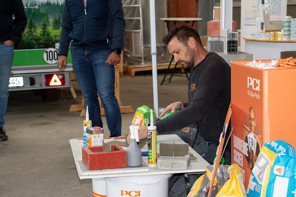 Ein PCI-Fachberater zeigt beim Kompetenztag in Aigen verschiedene Baustoffprodukte und deren praktische Anwendung an einem Vorführtisch.