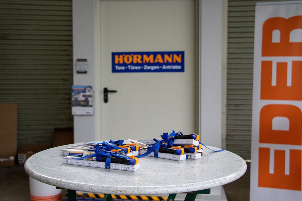 Werbematerialien und kleine Giveaways von Hörmann liegen auf einem Tisch vor einer ausgestellten Tür beim Kompetenztag für Profis in Aigen.